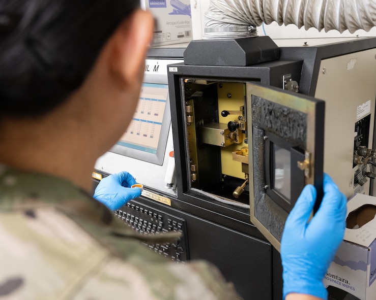 An Airman places a small container of engine oil into an analyzer machine.