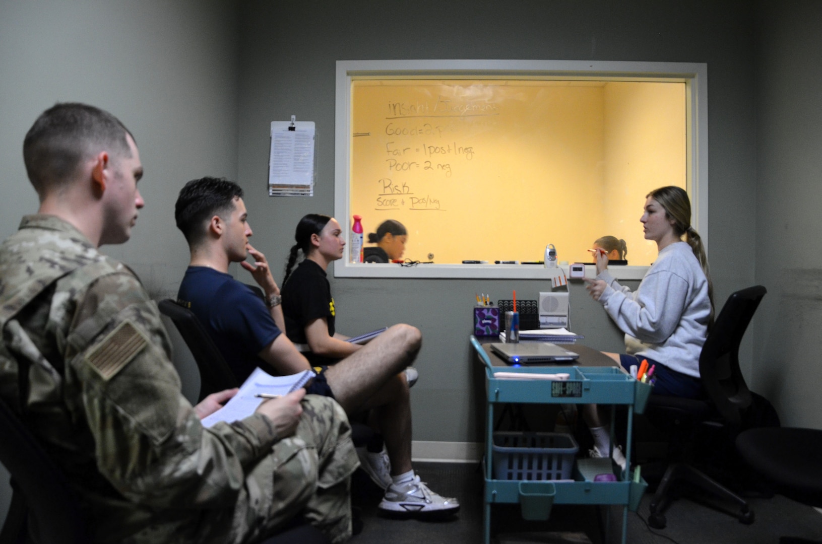 (Left to right) MHT students Airman Jeremy Estrada, Hospital Corpsman 3rd Class John Flores, and Pfc. Meriya Bowman and their instructor, Staff Sgt. Paige Smith, observe from behind a one-way mirror as fellow students Hospitalman Nicole Faye Salvado and Spc. Nancy Hernandez conduct a mock counseling session. Military MHTs serve a critical role within the Military Health System by providing clinical and administrative support to mental health providers that contributes to the readiness and resilience of the Joint Force. Located at the Medical Education and Training Campus on Joint Base San Antonio-Fort Sam Houston, Texas, the MHT course trains Army, Navy, Air Force, and Coast Guard students.