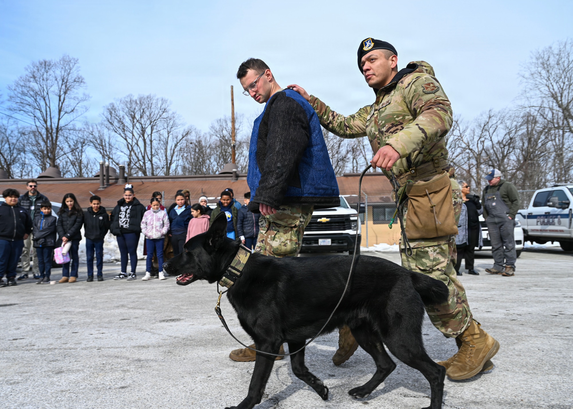 U.S. Air Force Staff Sgt. Alex Reza, 316th Security Support Squadron military working dog handler, right, conducts a military working dog demonstration for students from Patrick Henry K-8 School during a base tour at Joint Base Andrews, Maryland, Feb. 10, 2026. Students were able to visit the MWD flight and 316th Civil Engineer Squadron explosive ordnance disposal flight for a community engagement tour, hosting 46 students from a local school to gain a better understanding of the military. (U.S. Air Force photo by Staff Sgt. Aubree Owens)