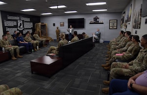 A man speaks to a group of people in military uniform.