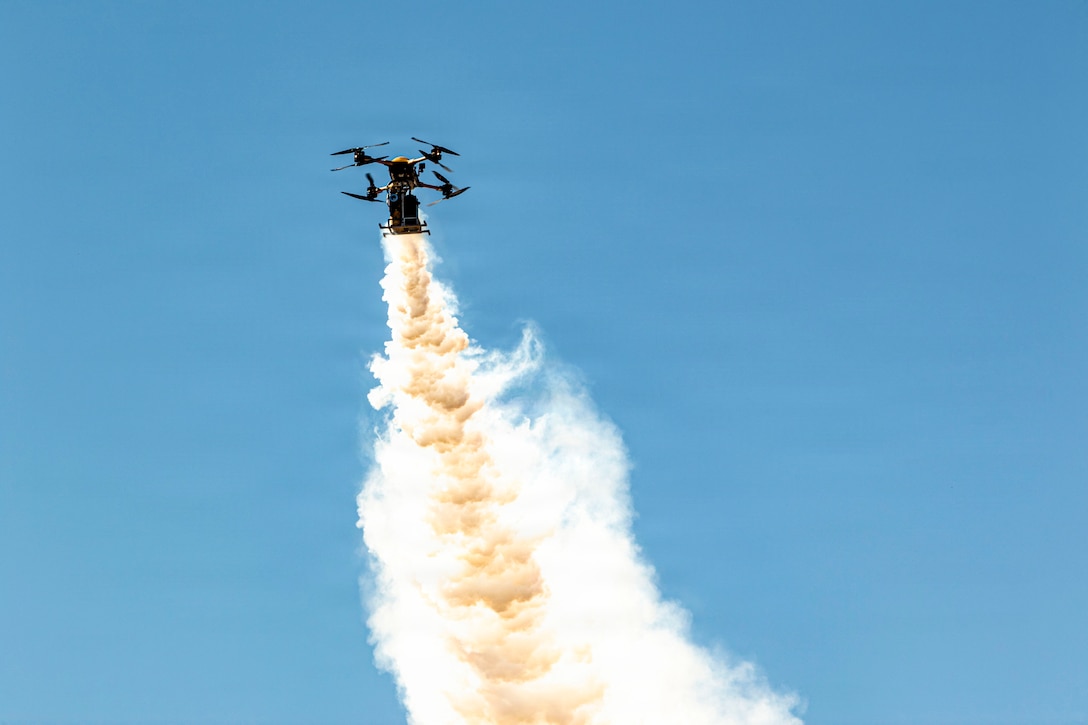Smoke emanates from the bottom of a four-propeller drone in blue sky.
