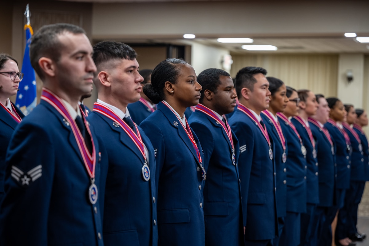 A formation of women and men in formal Air Force dress uniforms with red pendent ribbons around their necks