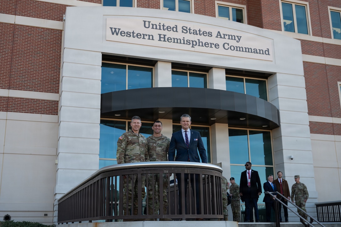 Secretary of War Pete Hegseth stands with two service members outside an Army Western Hemisphere Command building.