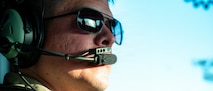 An Airman wearing sunglasses and headphones with a mic looks off camera, the cockpit is reflected in his glasses.