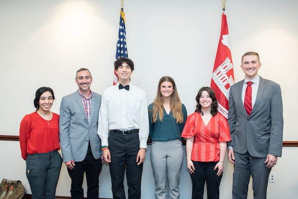a group of people stand in front of the US flag and USACE flags after an internship presentation