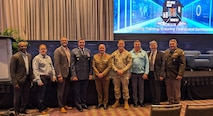 U.S. Indo-Pacific Command’s J7 Director, USAF Brig. Gen. Richard Goodman (fourth from left), and Dr. Andre Stridiron III (third from left), Pacific Multi Domain Training and Experimentation Capability program manager, stress the importance of realistic all-domain training during the 2025 Interservice/Industry Training, Simulation and Education Conference, December 4, in Orlando, Florida.