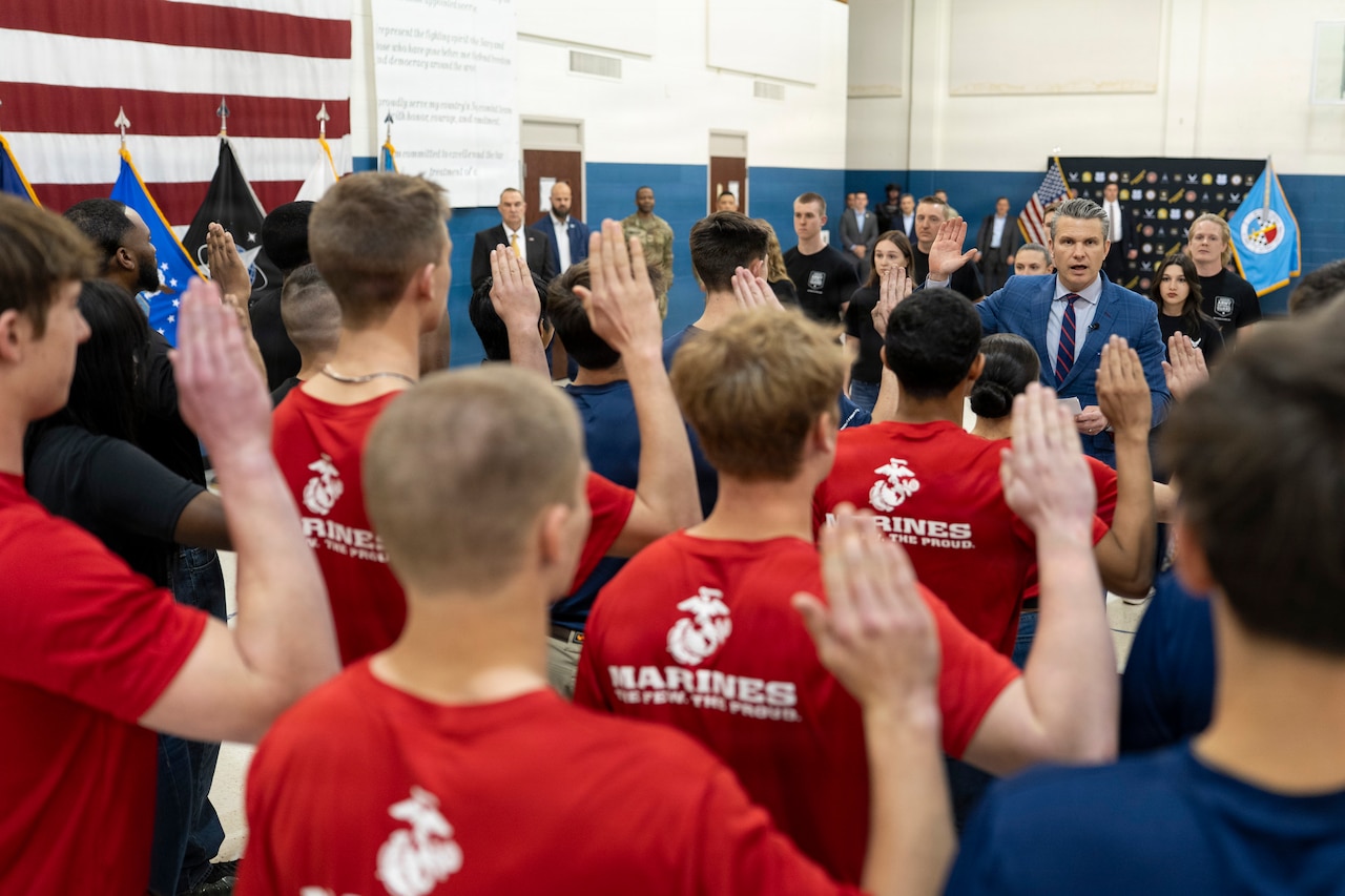 Future service members raise their right hands as the secretary of war delivers the oath of enlistment.