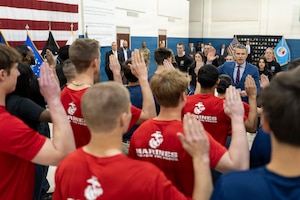 Future service members raise their right hands as a man in a business suit delivers the oath of enlistment in a large indoor room.
