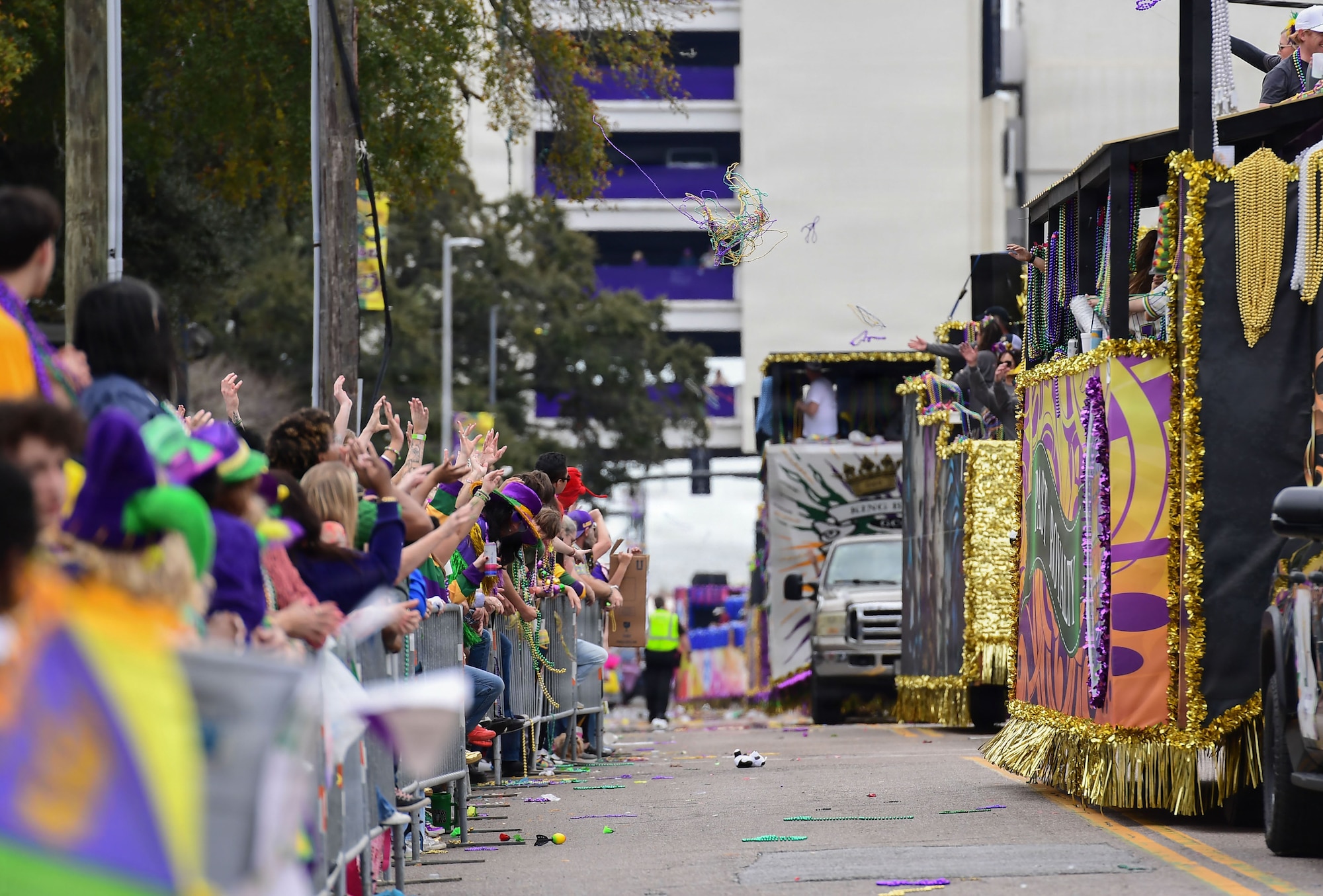 Parade floats make their way down the street while throwing beads to crowds.