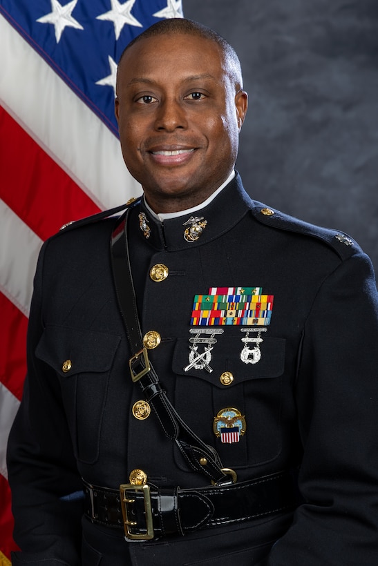 A dark-skinned man in a dress uniform for the Marine Corps. There is a flag behind him.