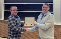 Airmen in civilian clothes hold a certificate.