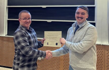Airmen in civilian clothes hold a certificate.
