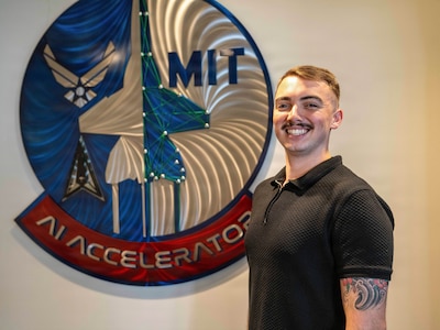 Airman poses for a photo in front of a sign.