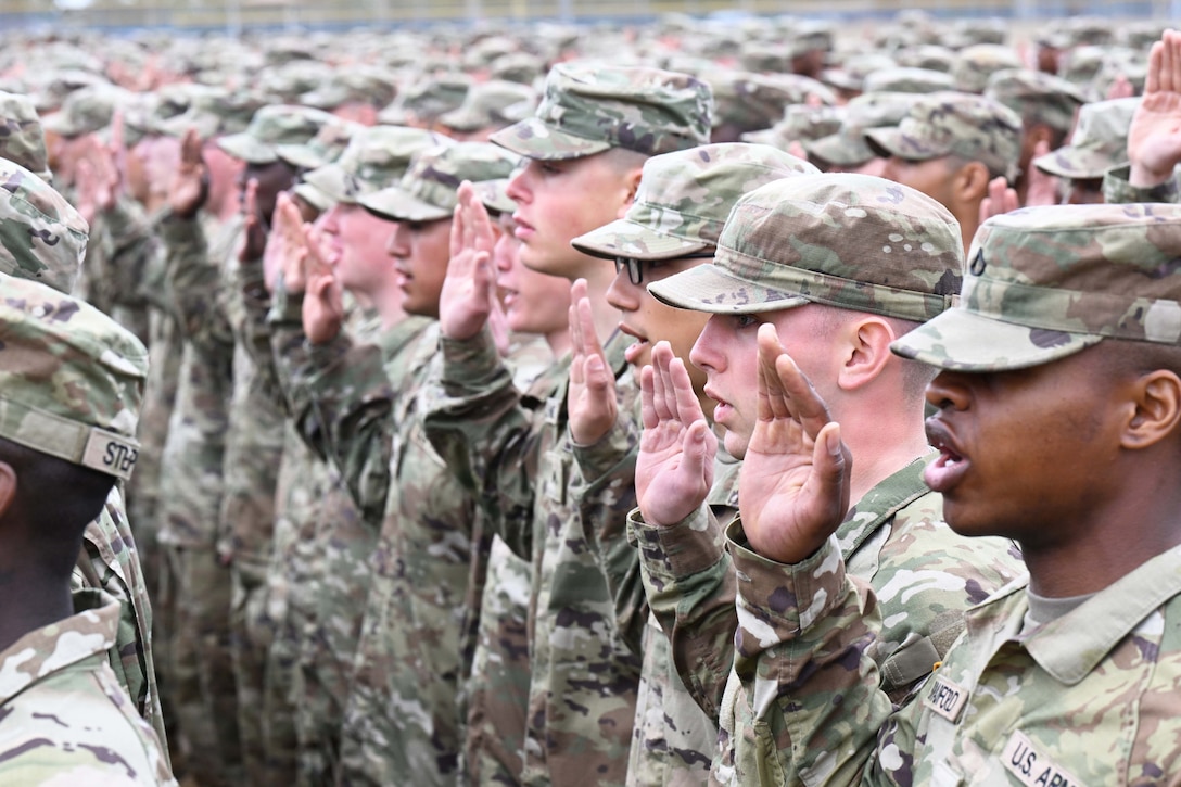 Dozens of soldiers standing in formation raise their right hands while reciting an oath.