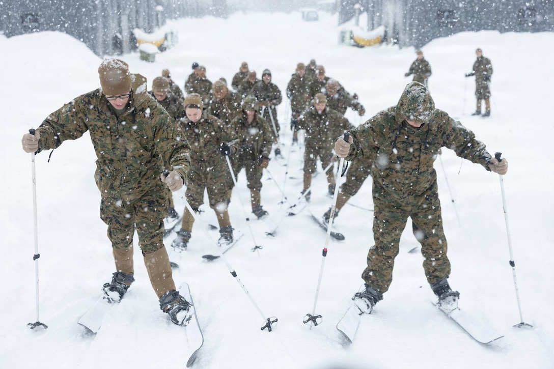 Heavy snow falls as Marines and sailors ski up a hill.