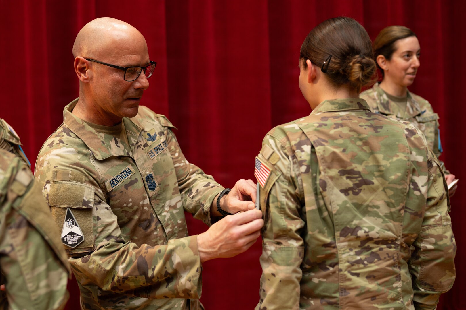 Chief Master Sergeant of the Space Force John Bentivegna places a new U.S. Space Force  patch on the uniform of graduating Space Force Spc. Shayla Town during a Basic Military Training patching ceremony at Bob Hope Theater, Joint Base San Antonio-Lackland, Texas, Feb. 17, 2026. The patching ceremony is the first graduation event and symbolizes the transition from trainee to Guardian, connecting the new Guardians to their service’s core values. CMSSF participated in the event before speaking to the graduates about the importance of their mission to dominate the space domain and secure our nation's future. (U.S. Air Force photo by Jonathan R. Mallard)