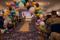 A speaker stands at the front of the room and is seen through a balloon arch in the back of the room.