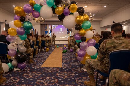 A speaker stands at the front of the room and is seen through a balloon arch in the back of the room.