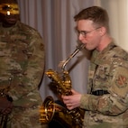 Airman plays baritone saxophone in camo uniform.