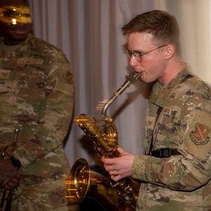 Airman plays baritone saxophone in camo uniform.