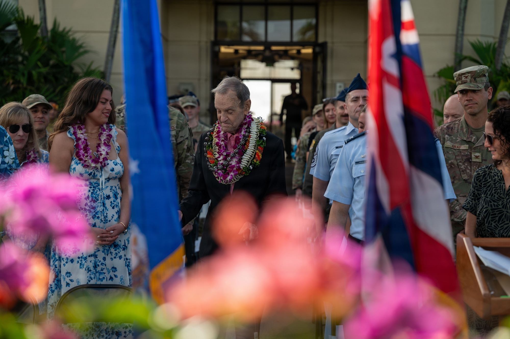 A man walks down an aisle to his seat while wearing Hawaiian leis.