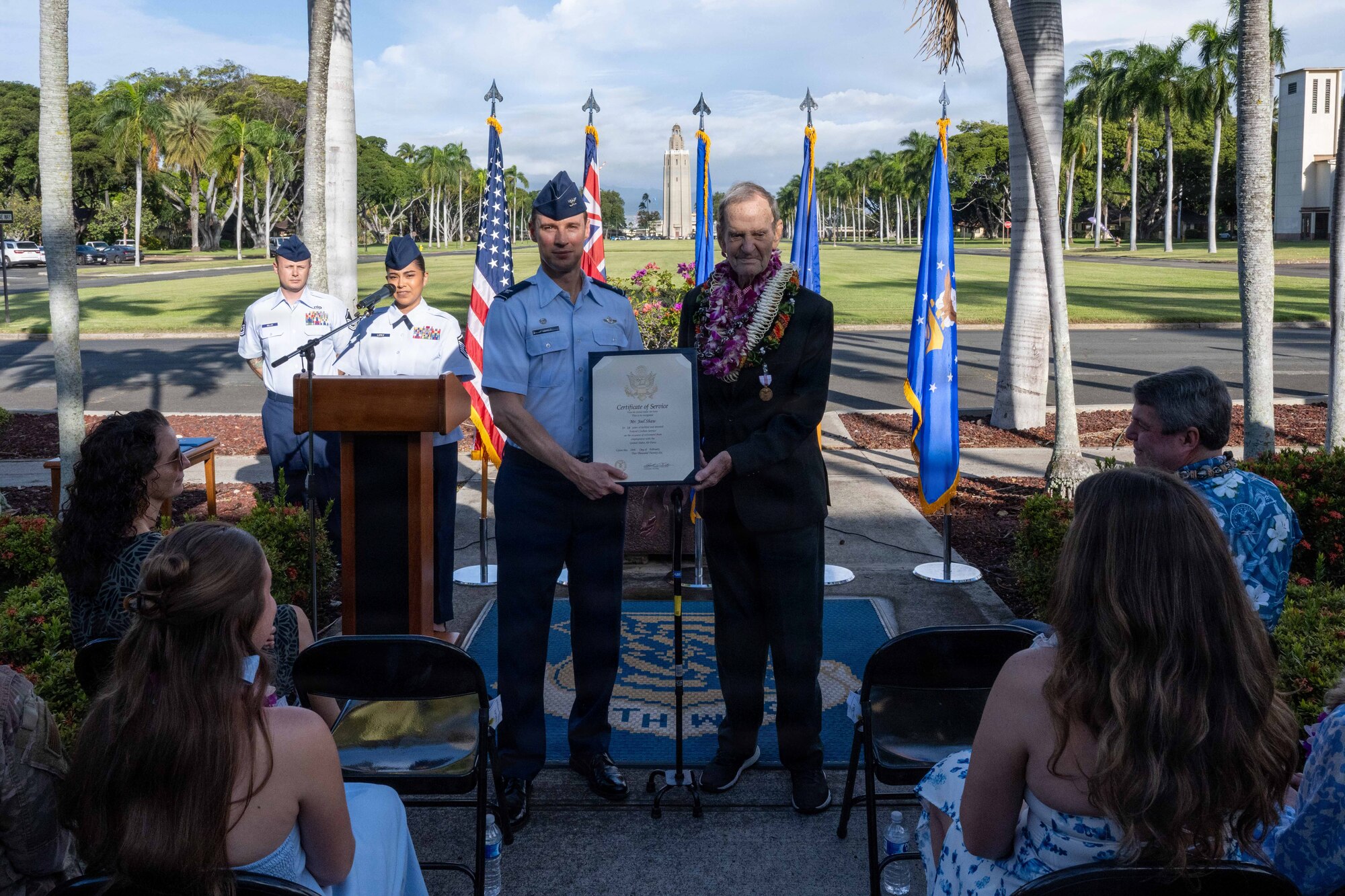 A U.S. Air Force Colonel and an elderly man hold a retirement certificate in front of a crowd.