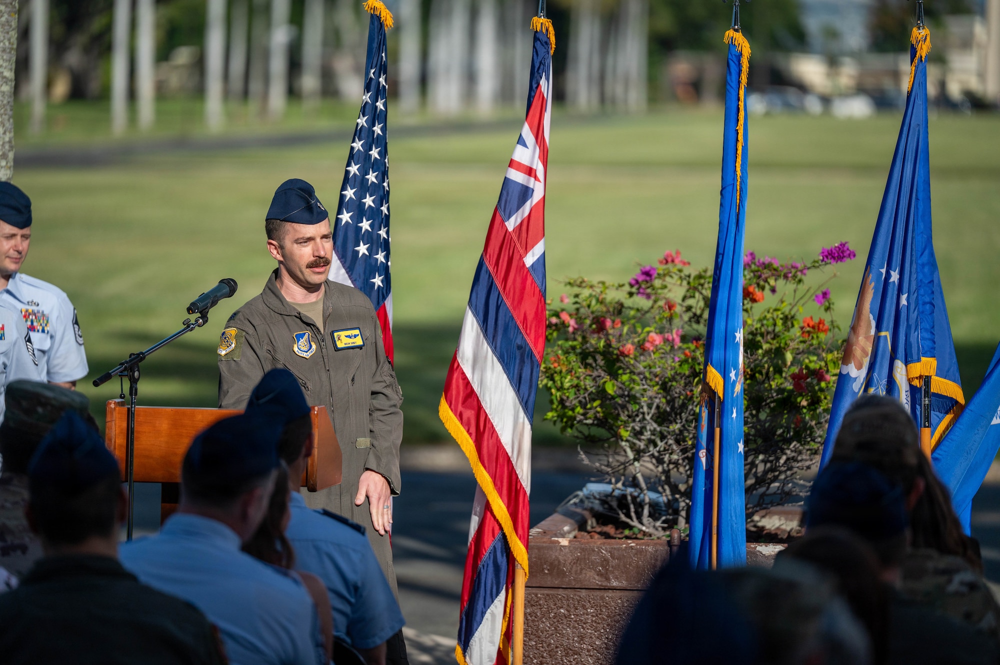 A man wearing a U.S. Air Force flight suit speaks to a crowd during a retirement ceremony.