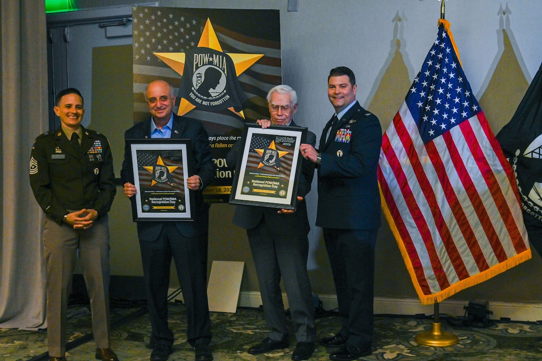 The Defense POW/MIA Accounting Agency Senior Enlisted Advisor, U.S. Army Sgt. Maj. Lauren Flores, and DPAA Chief of Staff, U.S. Air Force Col. Derek Rankin, stand alongside two former prisoners of the Vietnam War during the unveiling of the National POW/MIA Recognition Day poster at the Charleston Family Member Update, Feb. 21, 2026.