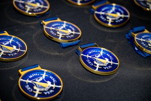 Blue medallions with a gold rim, inlaid with a unit emblem, are laid on a black table