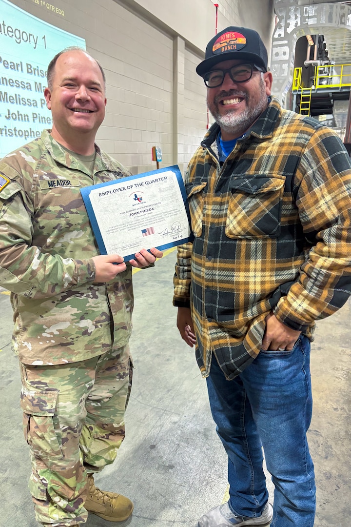 A man wearing a camouflage military uniform poses with another person holding an award certificate.