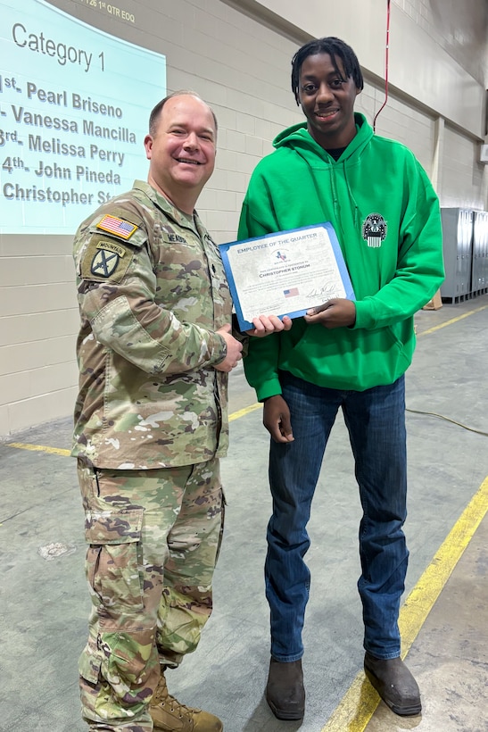 A man wearing a camouflage military uniform poses with another person holding an award certificate.