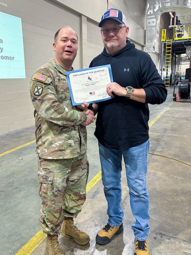 A man wearing a camouflage military uniform poses with another person holding an award certificate.