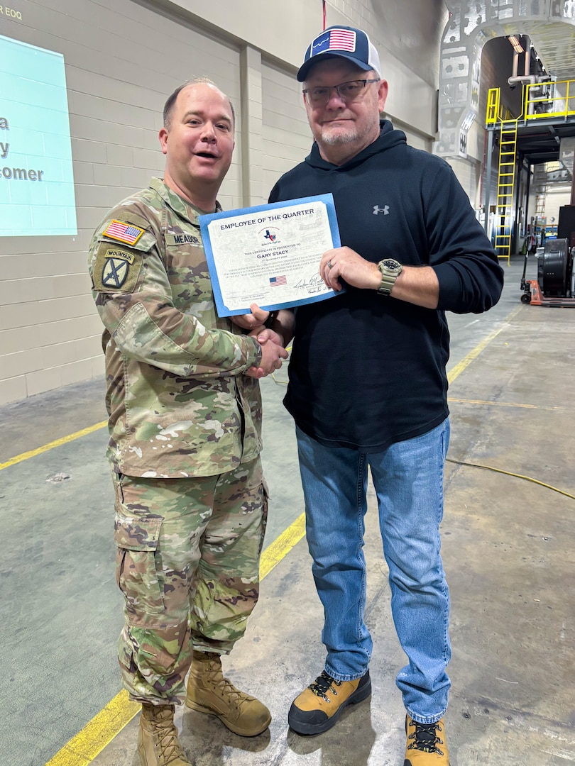 A man wearing a camouflage military uniform poses with another person holding an award certificate.