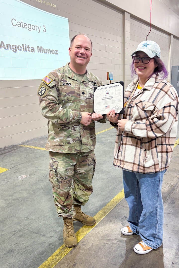 A man wearing a camouflage military uniform poses with another person holding an award certificate.