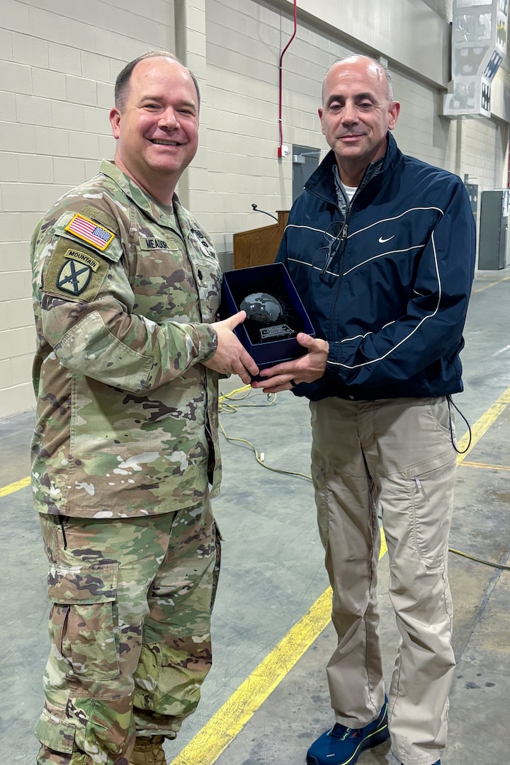 A man wearing a camouflage military uniform poses with another person holding a trophy.