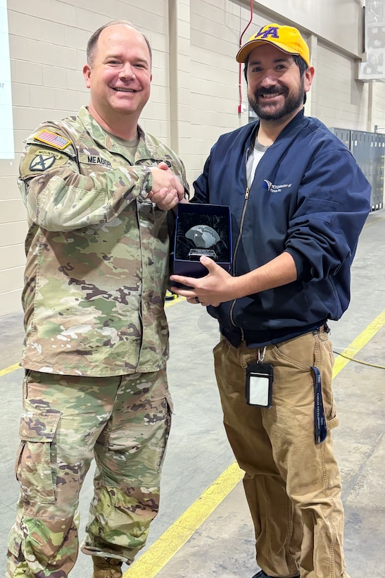 A man wearing a camouflage military uniform poses with another person holding a trophy.