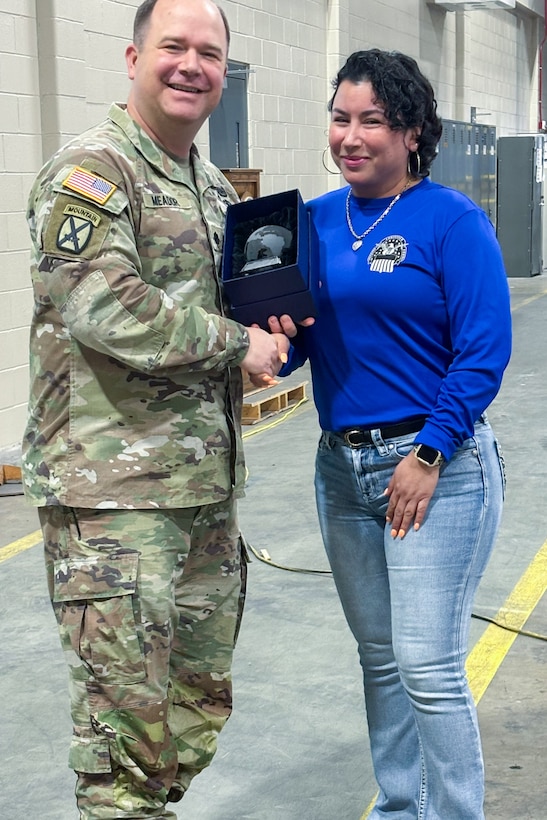 A man wearing a camouflage military uniform poses with another person holding a trophy.