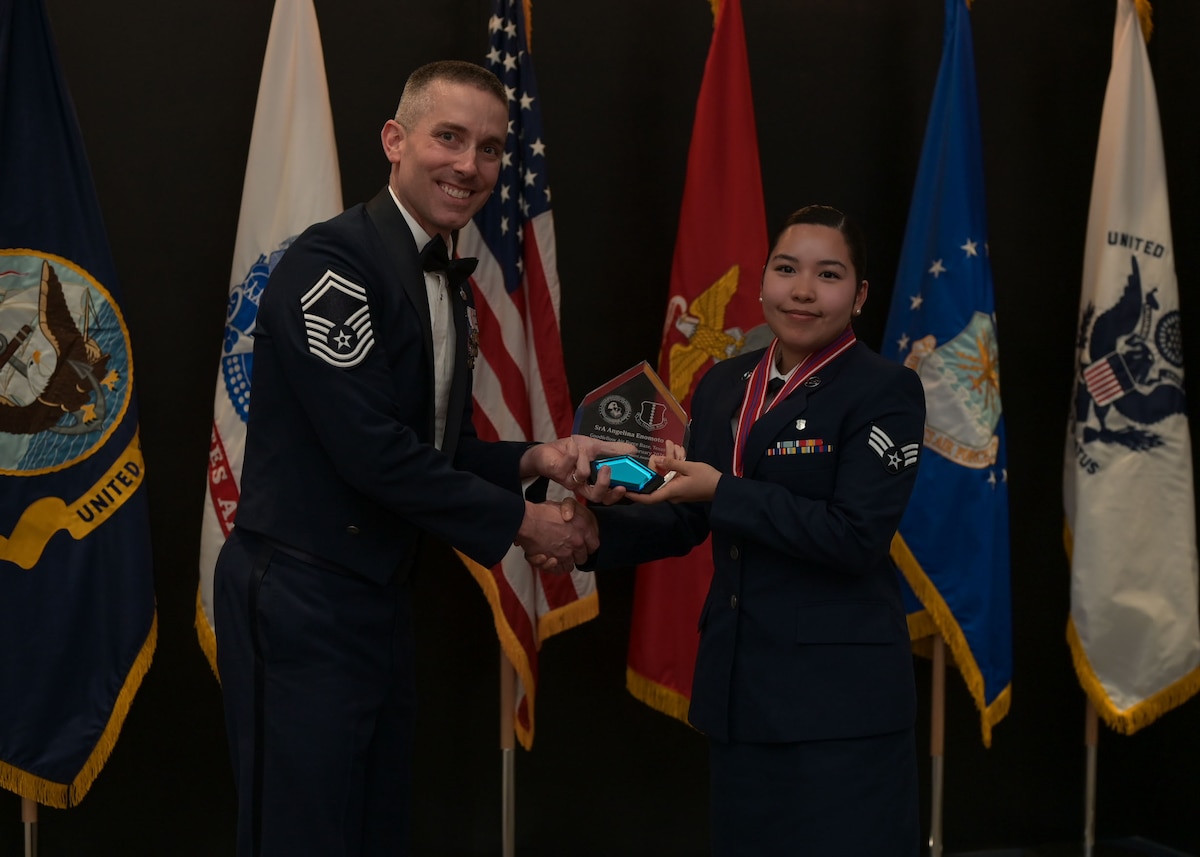 An Air Force senior master sergeant presents a glass plaque to a senior airman for an academic award.