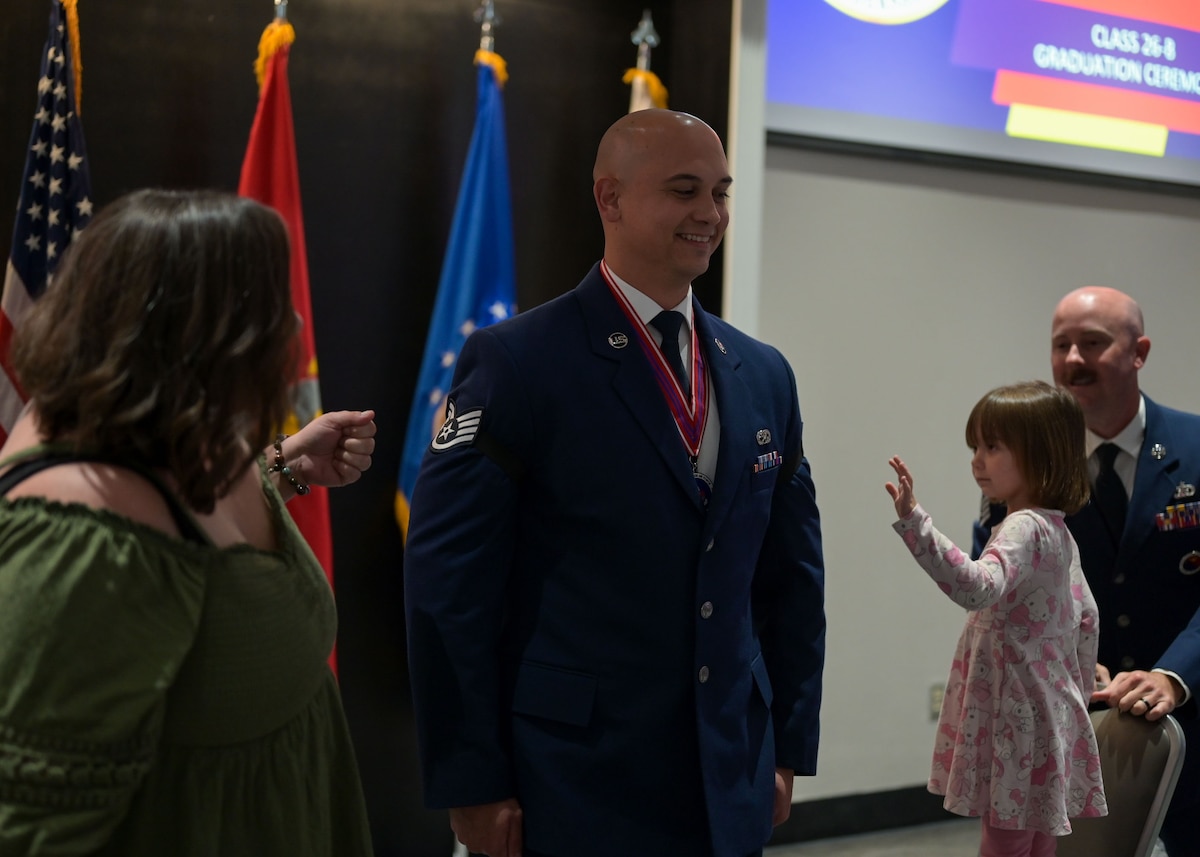 An Air Force senior airman is standing up with his daughter and wife to his sides, as they prepare to pin on his new rank.