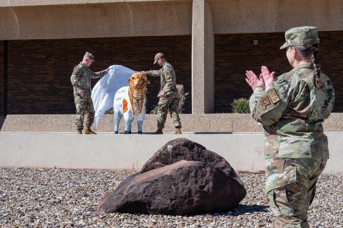 Two service members unveiling a statue of a sheep.
