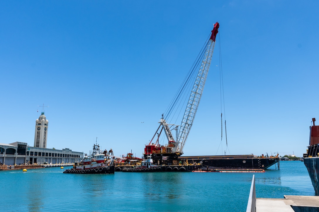 A barge with a crane on top sits in the waters of Honolulu Harbor