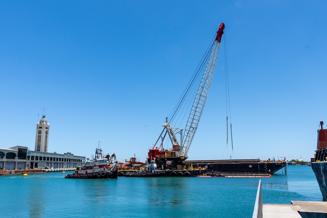 A barge with a crane on top sits in the waters of Honolulu Harbor