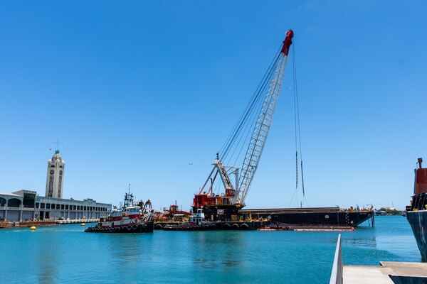 A barge with a crane on top sits in the waters of Honolulu Harbor
