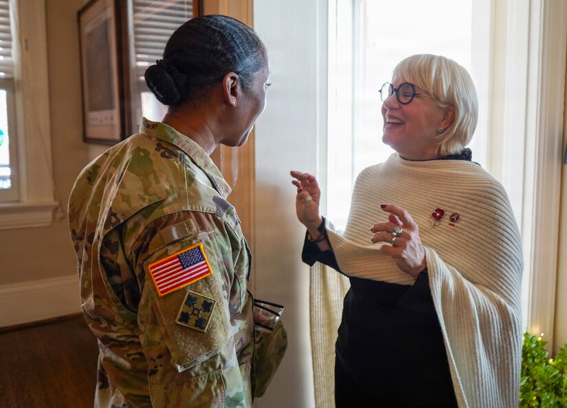 An Army Soldier in combat uniform is facing away from the camera, standing with a woman in civilian clothes who is gesturing and smiling while talking.
