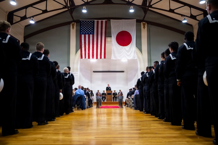 U.S. Navy Cmdr. Paul Archer, off-going commanding officer of Arleigh Burke-class guided-missile destroyer USS Preble (DDG 88), center, delivers remarks to guests and assembled crew members during a change of command ceremony at Commander, Fleet Activities Yokosuka Headquarters’ C-2 Auditorium in Yokosuka, Japan, Feb. 20, 2026.
