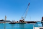 A barge with a crane on top sits in the waters of Honolulu Harbor
