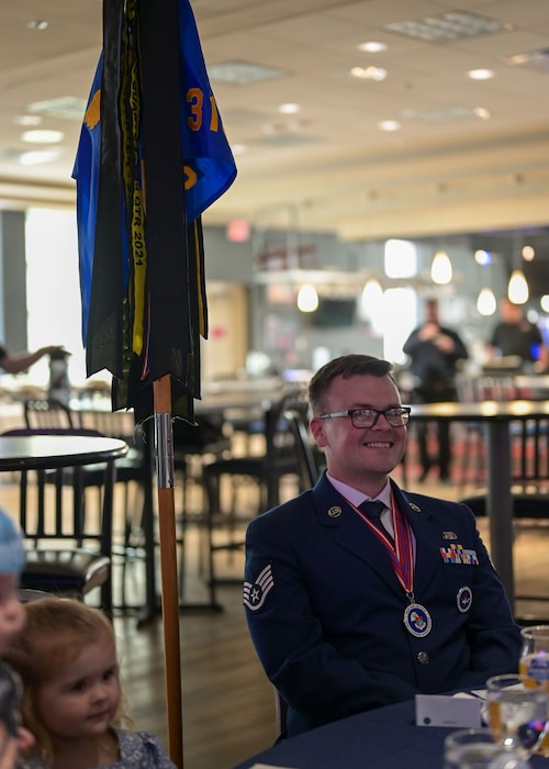 An Air Force staff sergeant sits at a table, smiling during a semi-formal ceremony.