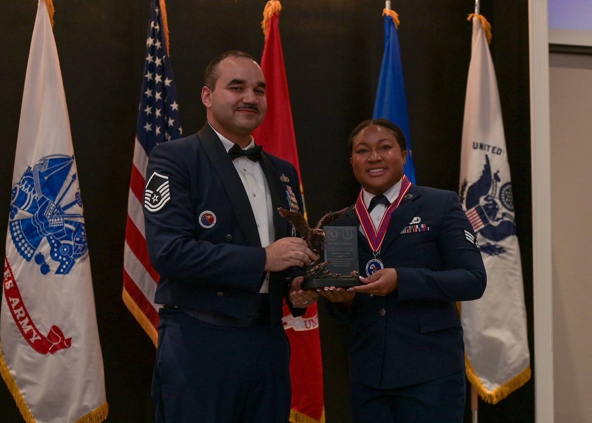 An Air Force master sergeant presents a bronze eagle statue to a senior airman for an award.