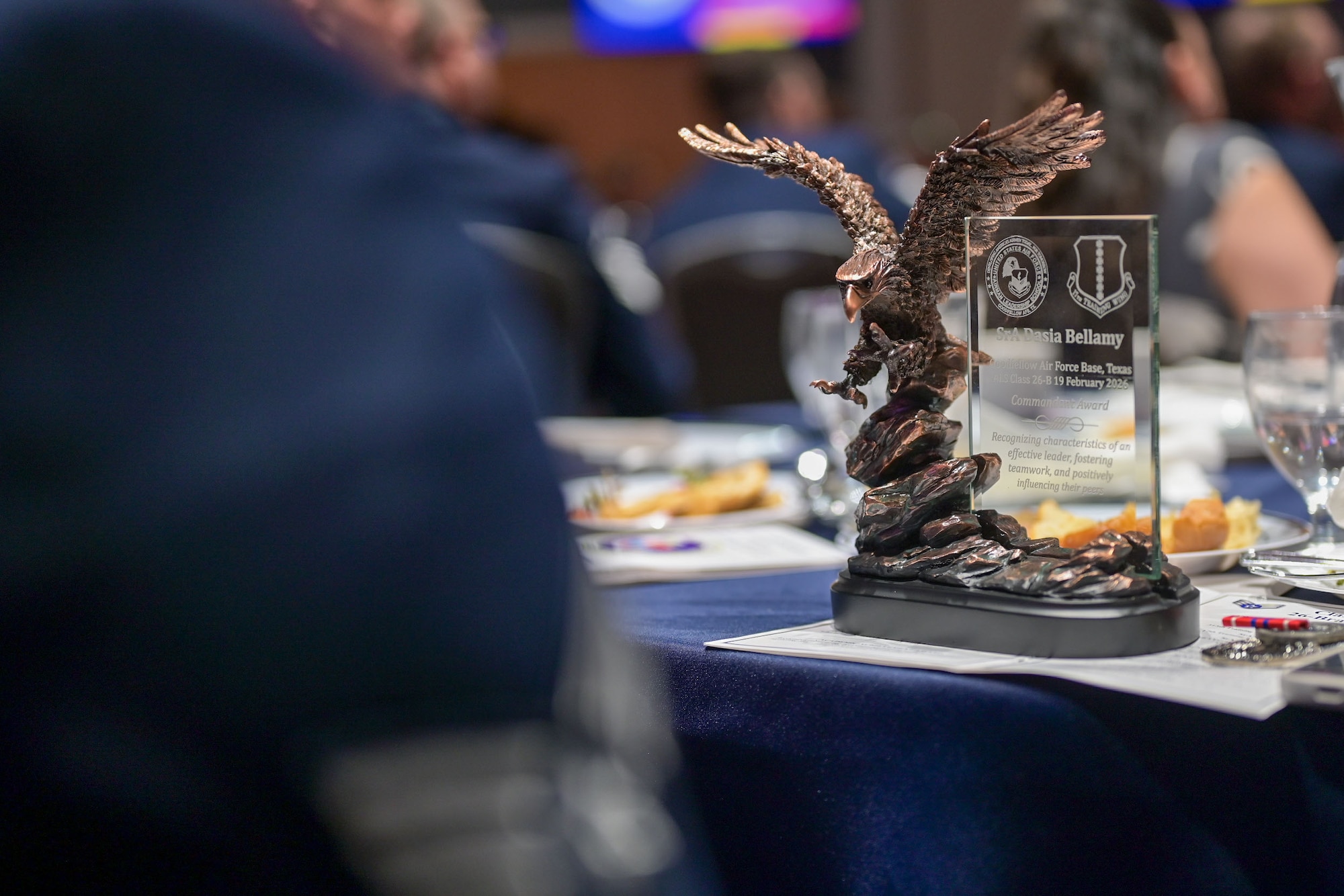 A bronze eagle statue attached to a glass plaque sits in focus, reading the name of the award recipient.