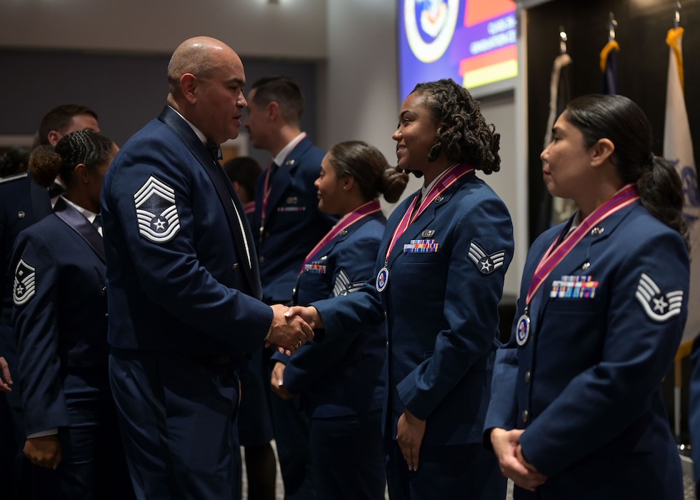 A chief master sergeant goes down a line of people, shaking the hands of a senior airmen at the end of a ceremony.